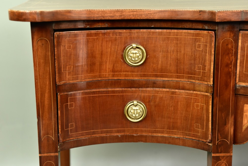 A Regency mahogany serpentine sideboard featuring curved drawer fronts, floral marquetry inlay, cast brass ring handles, and six tapered legs. View VI