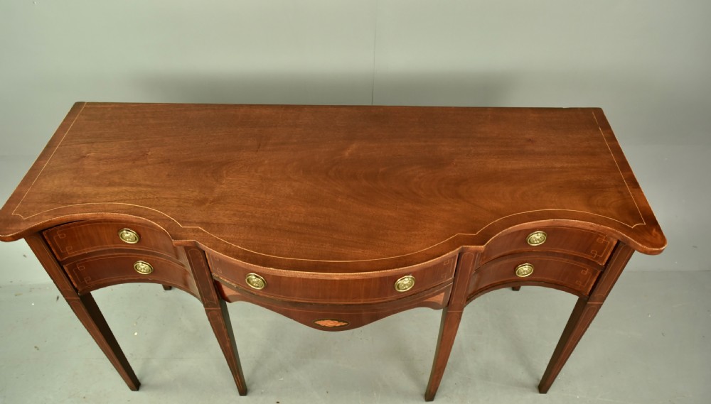 A Regency mahogany serpentine sideboard featuring curved drawer fronts, floral marquetry inlay, cast brass ring handles, and six tapered legs. View VII