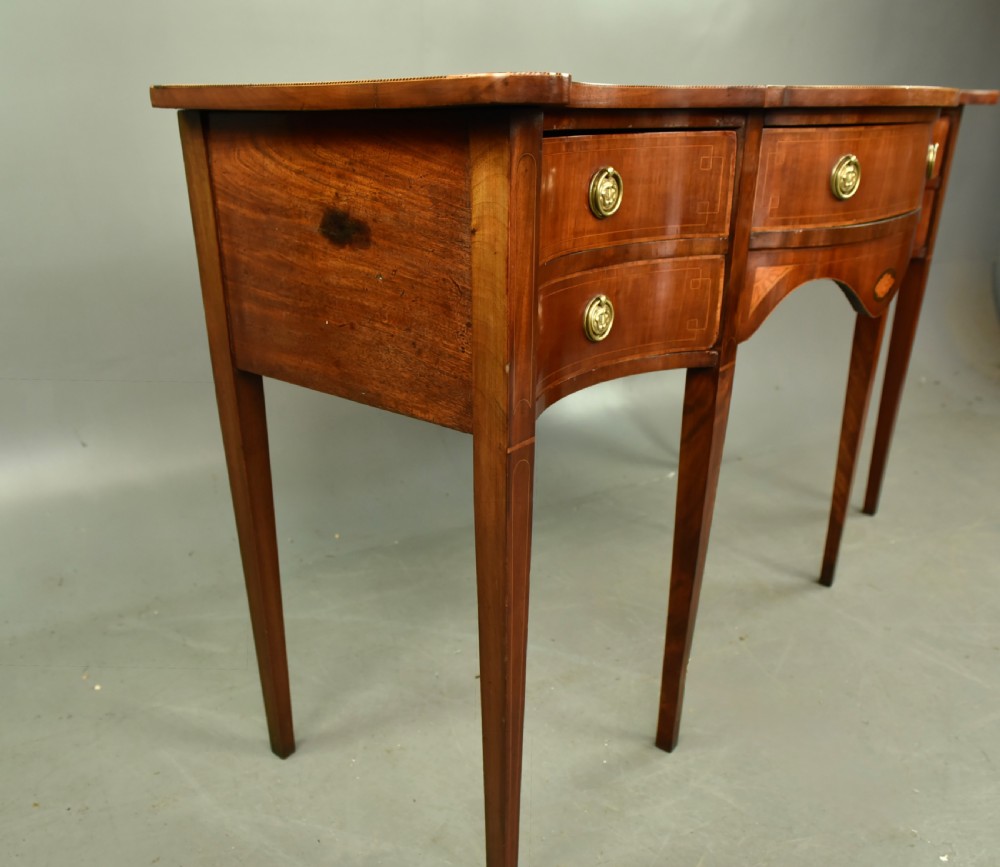 A Regency mahogany serpentine sideboard featuring curved drawer fronts, floral marquetry inlay, cast brass ring handles, and six tapered legs. View X