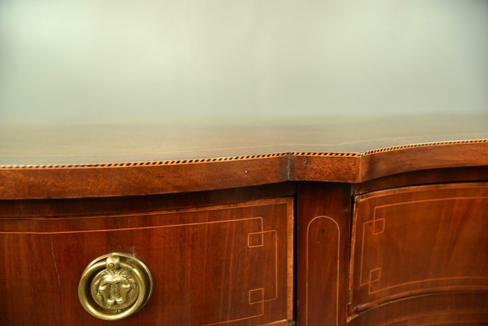 A Regency mahogany serpentine sideboard featuring curved drawer fronts, floral marquetry inlay, cast brass ring handles, and six tapered legs. View XI