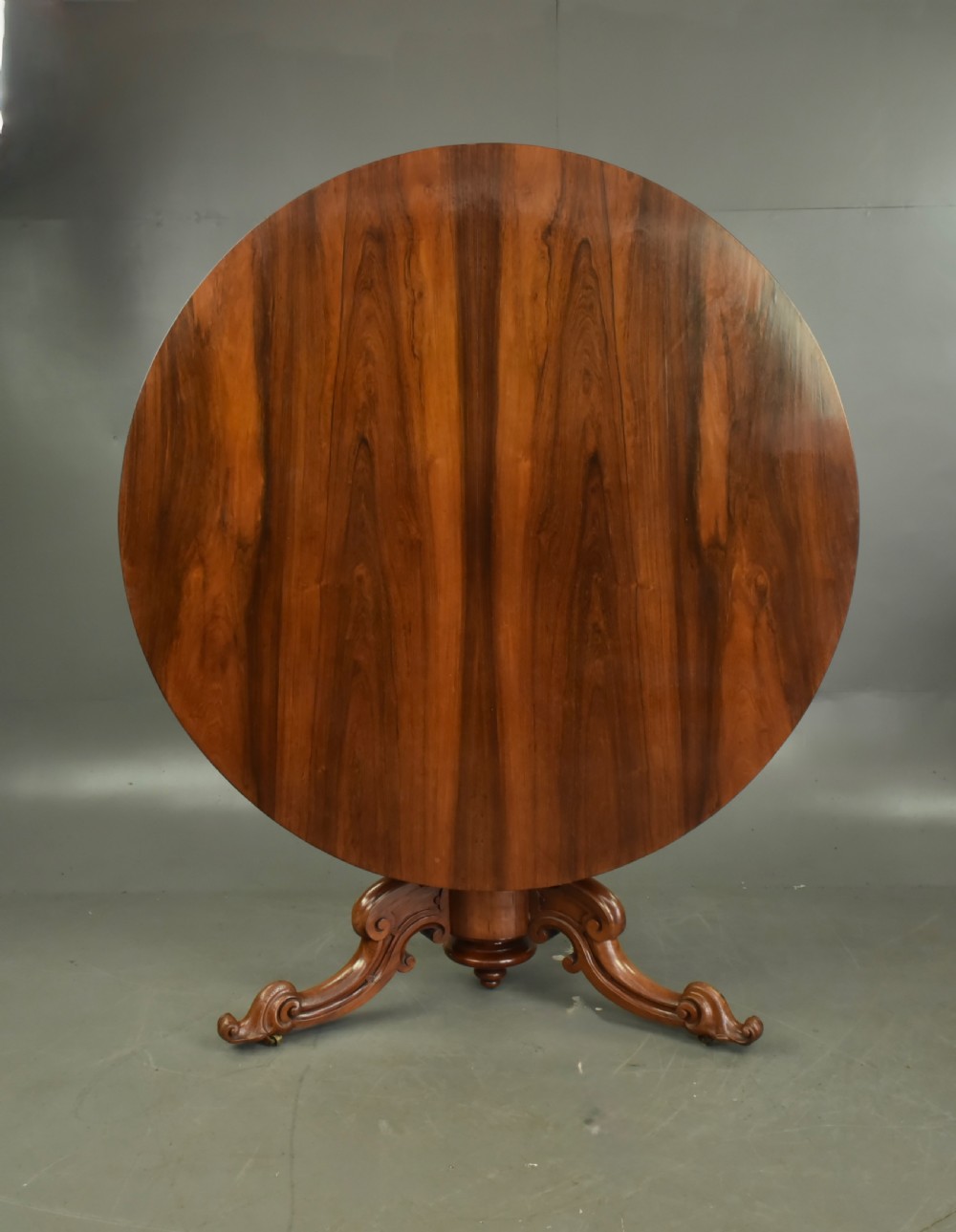 A round Victorian rosewood centre dining table featuring a figured timber top and a carved tripartite pedestal base.