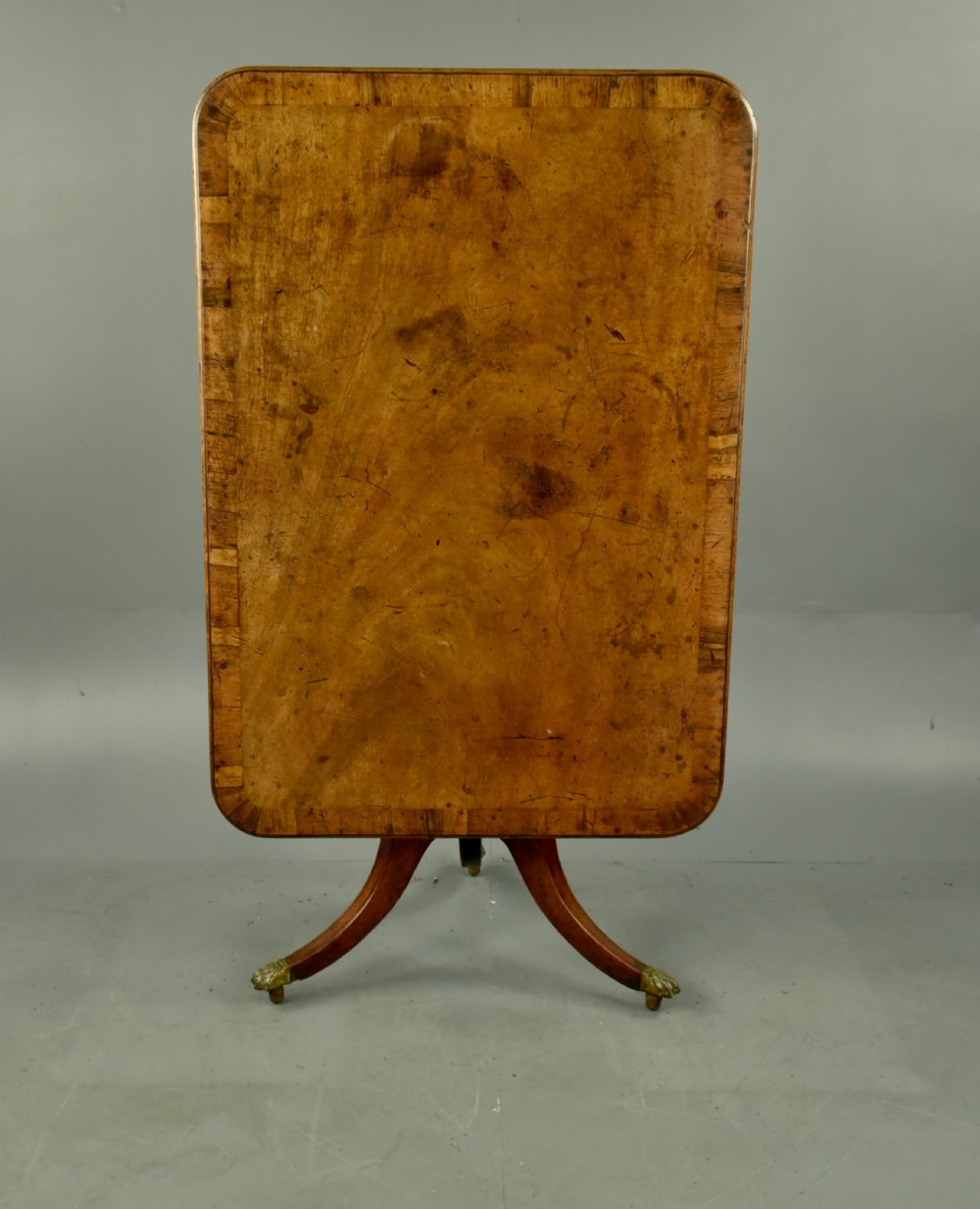 A Georgian mahogany tilt-top supper table with satinwood crossbanding set vertically on a swept tripod base with brass paw feet.