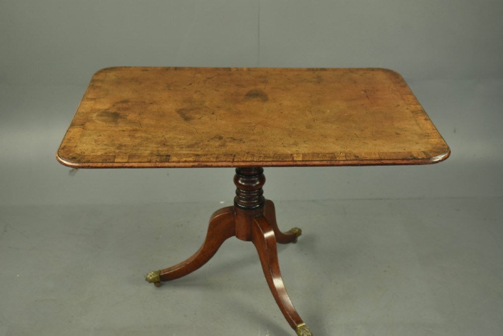 A Georgian mahogany tilt-top supper table with satinwood crossbanding set vertically on a swept tripod base with brass paw feet. View III