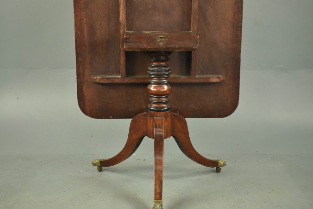 A Georgian mahogany tilt-top supper table with satinwood crossbanding set vertically on a swept tripod base with brass paw feet. View V