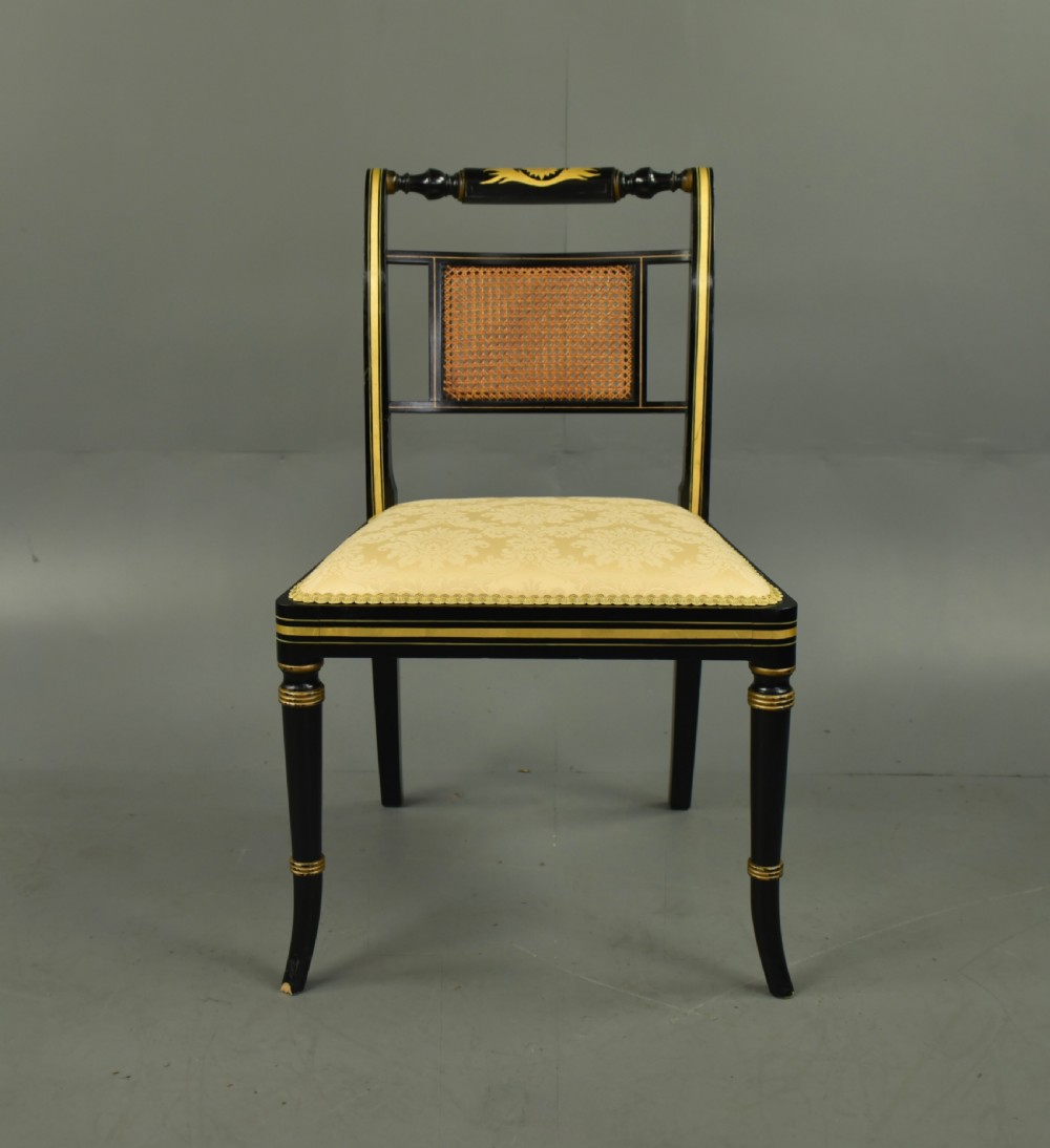 A set of six ebonised Regency dining chairs with gilt line decoration, woven cane back panels, and cream fabric seats. View II