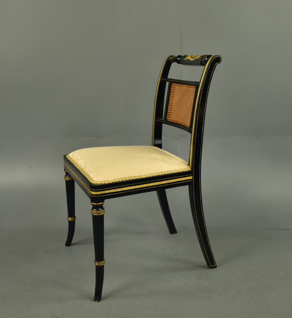 A set of six ebonised Regency dining chairs with gilt line decoration, woven cane back panels, and cream fabric seats. View III