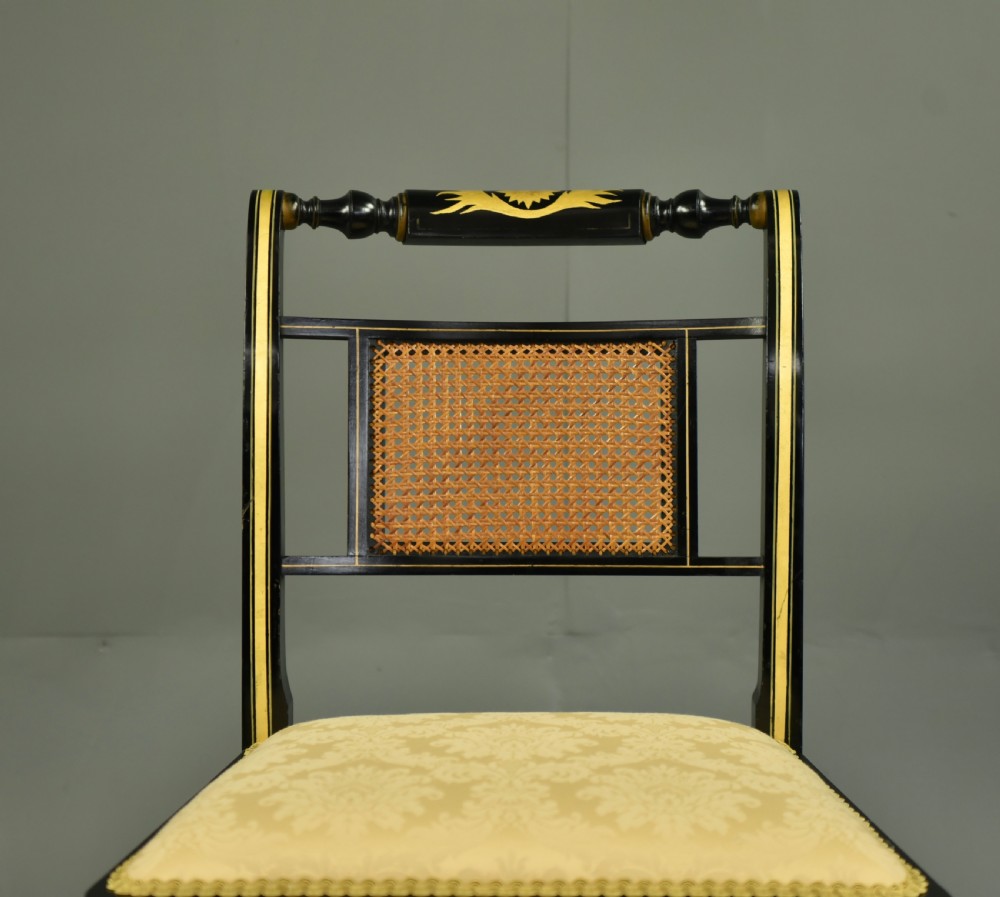A set of six ebonised Regency dining chairs with gilt line decoration, woven cane back panels, and cream fabric seats. View IV