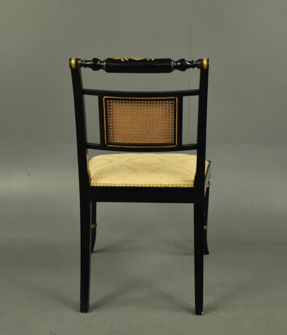 A set of six ebonised Regency dining chairs with gilt line decoration, woven cane back panels, and cream fabric seats. View V