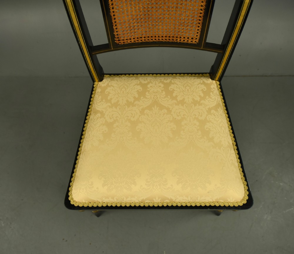 A set of six ebonised Regency dining chairs with gilt line decoration, woven cane back panels, and cream fabric seats. View VII