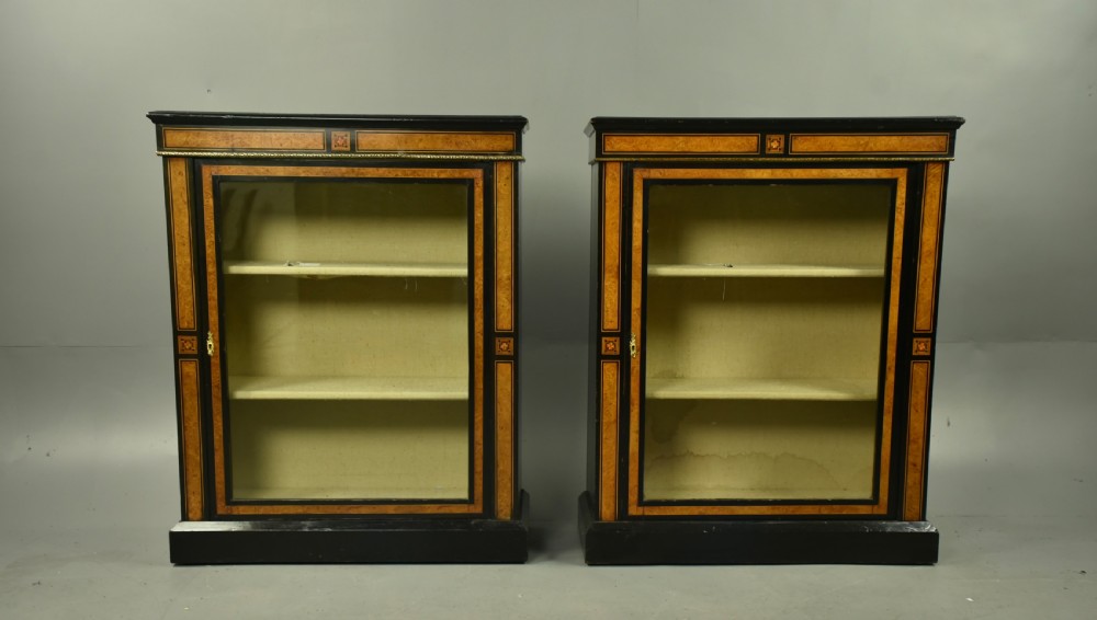 A pair of Victorian ebonised and burr walnut pier cabinets with glass doors, marquetry borders, and internal shelving.