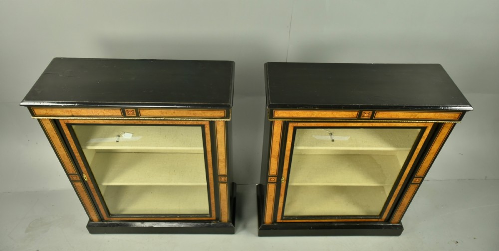 A pair of Victorian ebonised and burr walnut pier cabinets with glass doors, marquetry borders, and internal shelving. View VII
