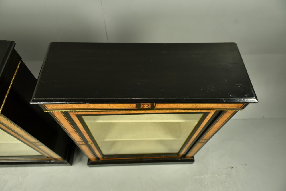 A pair of Victorian ebonised and burr walnut pier cabinets with glass doors, marquetry borders, and internal shelving. View IX