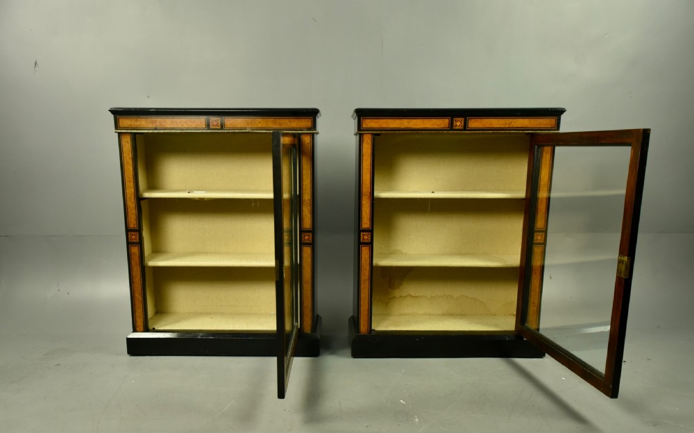 A pair of Victorian ebonised and burr walnut pier cabinets with glass doors, marquetry borders, and internal shelving. View X