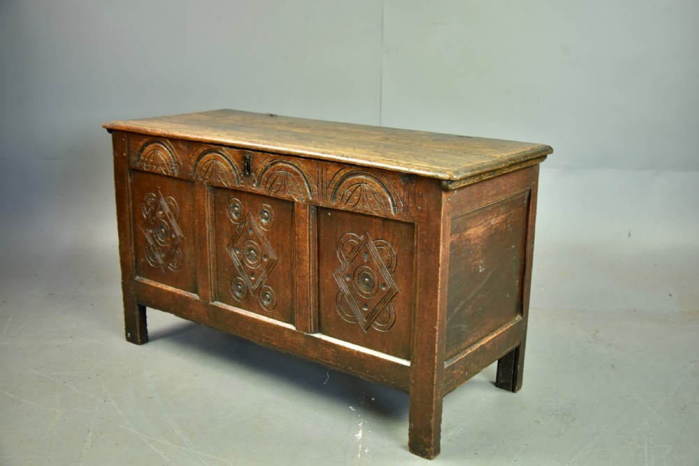 An 18th-century dark oak coffer featuring three carved geometric front panels and a carved lunette frieze resting on stile feet. View II