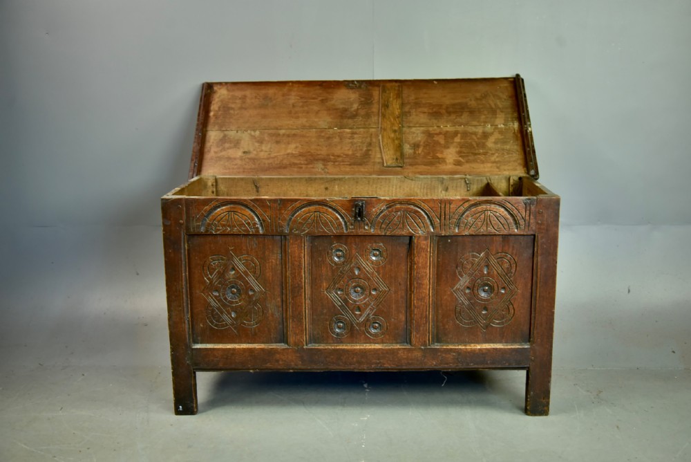 An 18th-century dark oak coffer featuring three carved geometric front panels and a carved lunette frieze resting on stile feet. View V