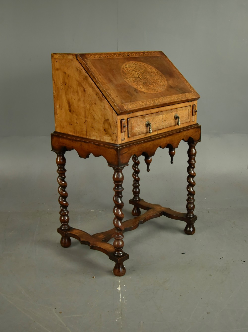 A small walnut bureau featuring an oval floral marquetry panel on the sloped front, set above a drawer and supported by four barley twist legs. View V