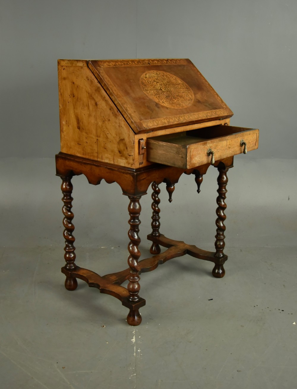 A small walnut bureau featuring an oval floral marquetry panel on the sloped front, set above a drawer and supported by four barley twist legs. View VI