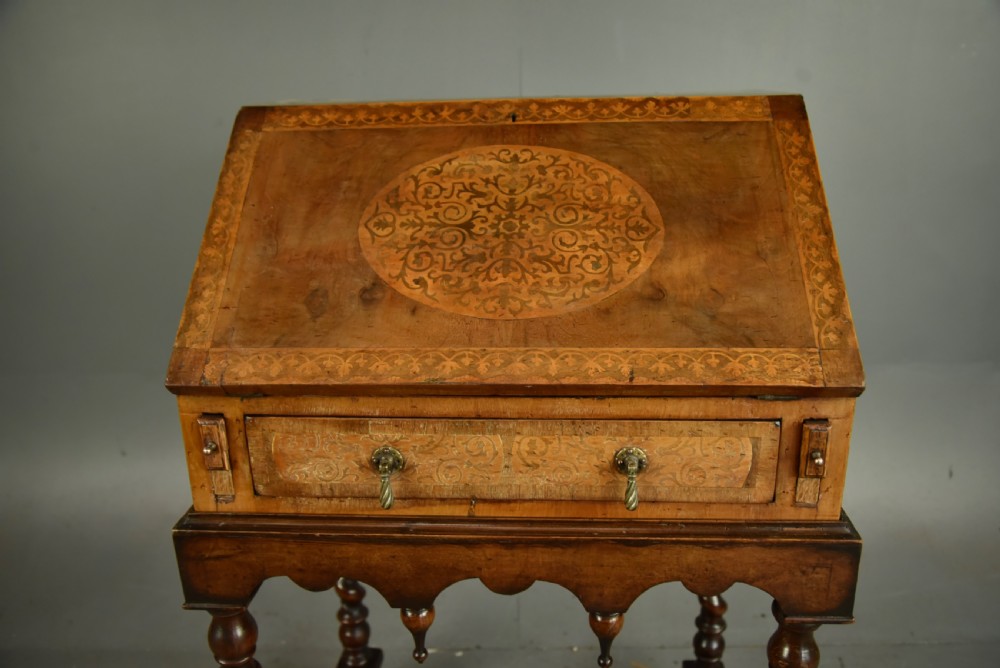 A small walnut bureau featuring an oval floral marquetry panel on the sloped front, set above a drawer and supported by four barley twist legs. View VII