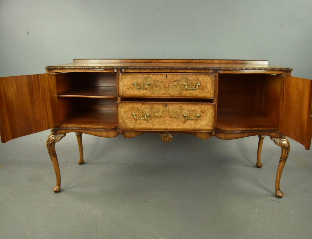 A Queen Anne style burr walnut sideboard featuring central drawers, flanking cupboard doors, carved shell detail, and cabriole legs. View V