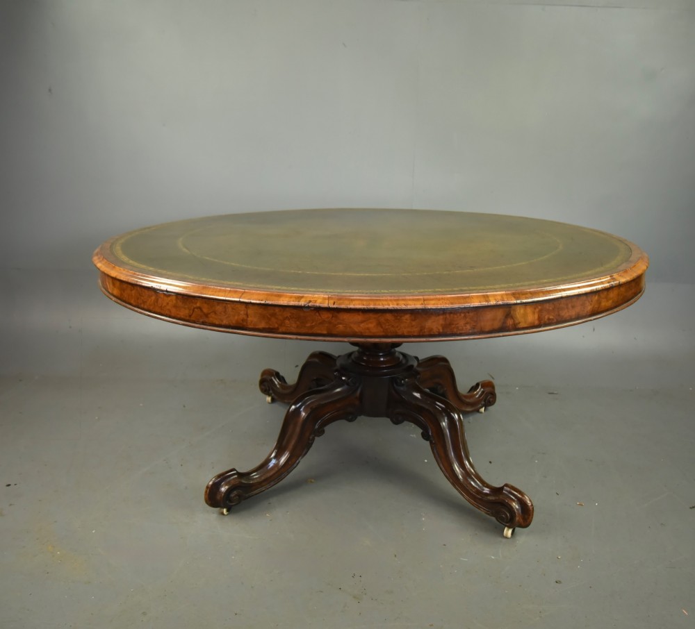 A large 19th-century circular Victorian walnut centre table featuring a green gilt-tooled leather inset writing surface and a carved pedestal base with four scroll legs on castors.