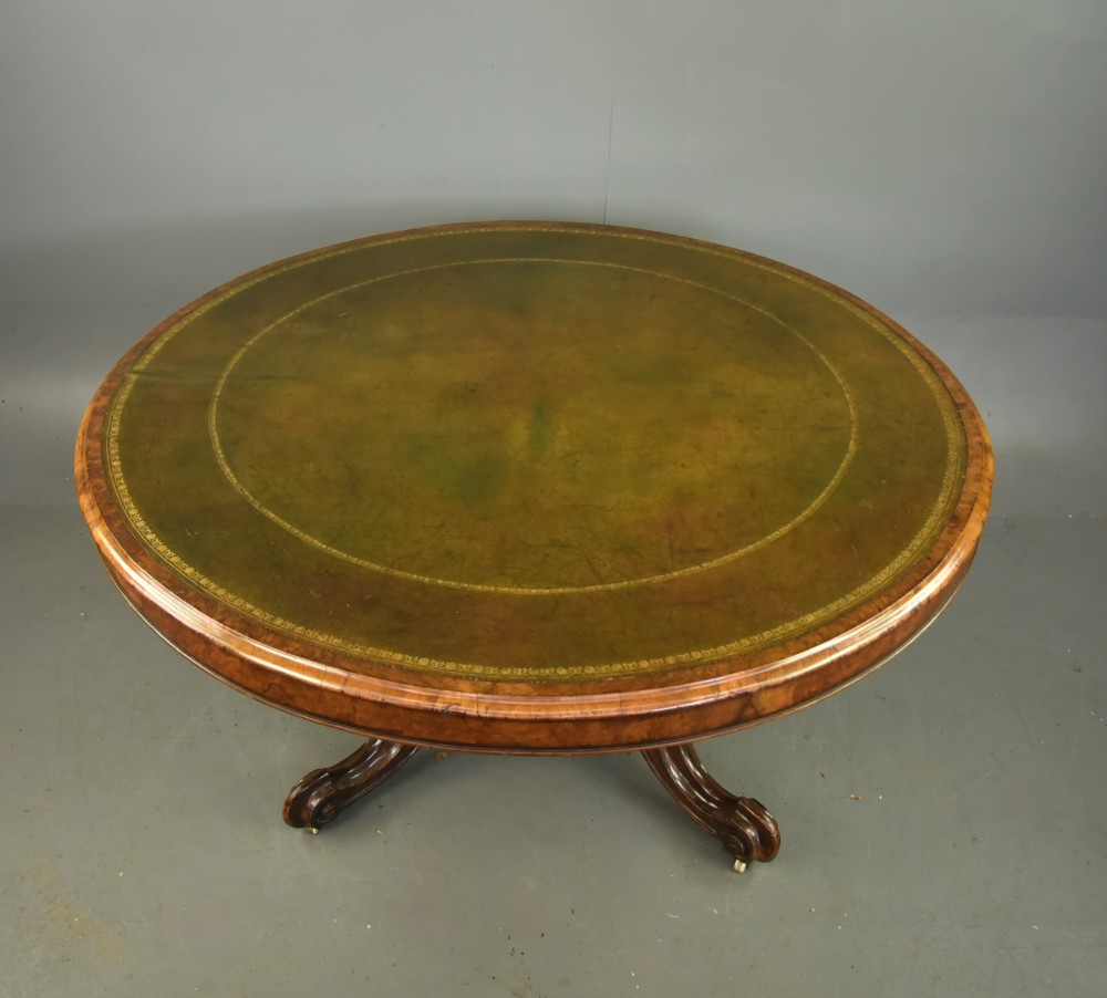 A large 19th-century circular Victorian walnut centre table featuring a green gilt-tooled leather inset writing surface and a carved pedestal base with four scroll legs on castors. View II