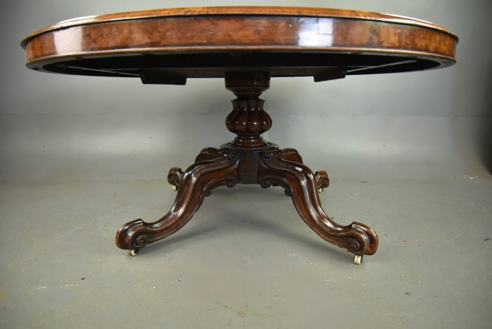A large 19th-century circular Victorian walnut centre table featuring a green gilt-tooled leather inset writing surface and a carved pedestal base with four scroll legs on castors. View V