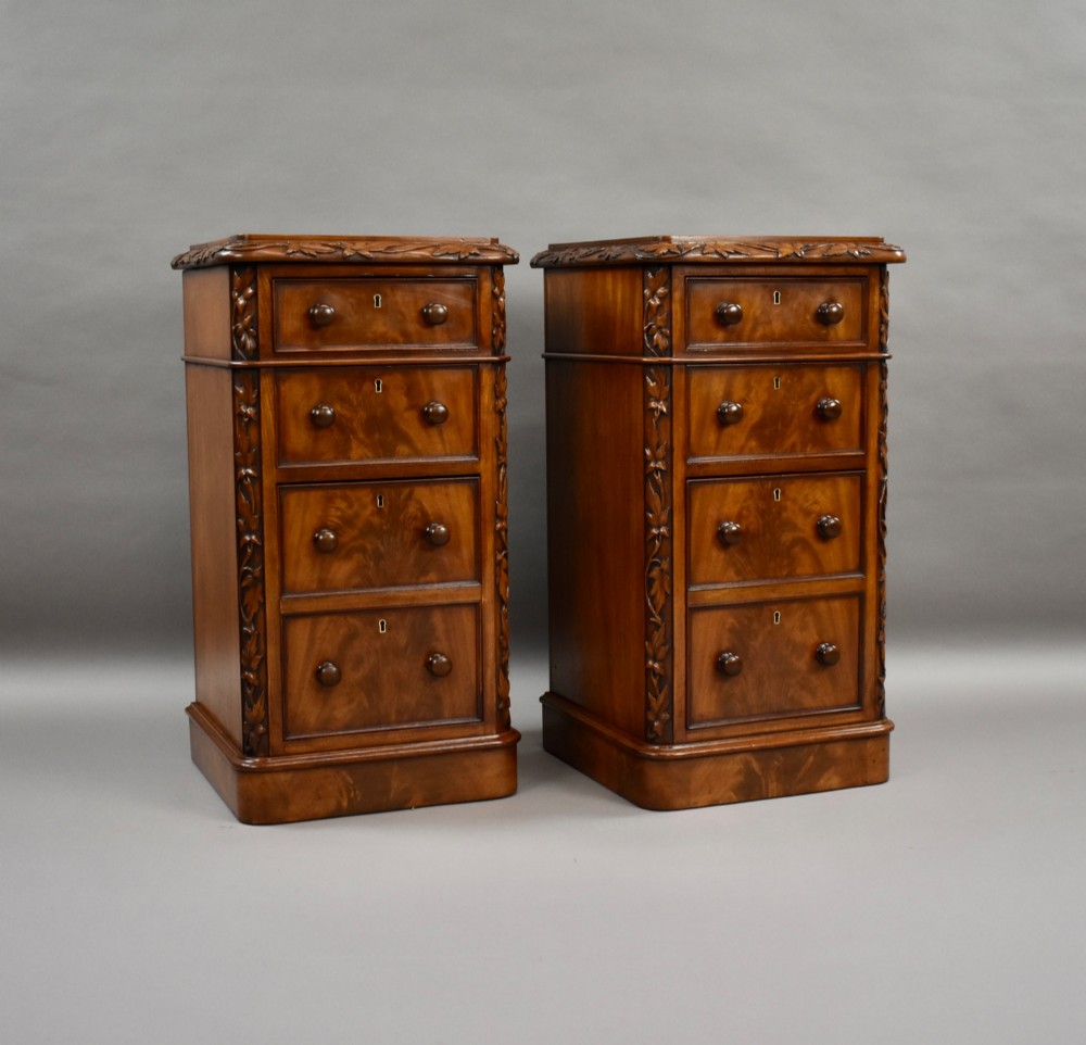 A pair of tall Victorian mahogany bedside chests with four drawers each, carved foliate columns, and turned wooden knobs on plinth bases.