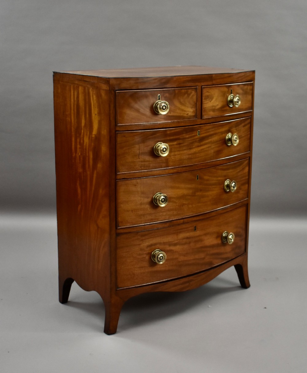 A narrow Regency mahogany bowfront chest featuring two short over three long drawers with turned brass handles and splayed bracket feet.