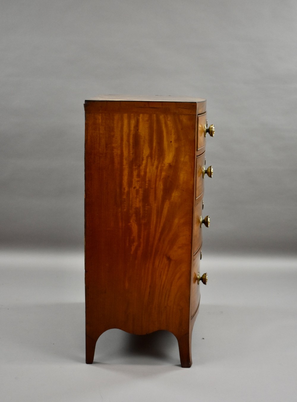 A narrow Regency mahogany bowfront chest featuring two short over three long drawers with turned brass handles and splayed bracket feet. View VII