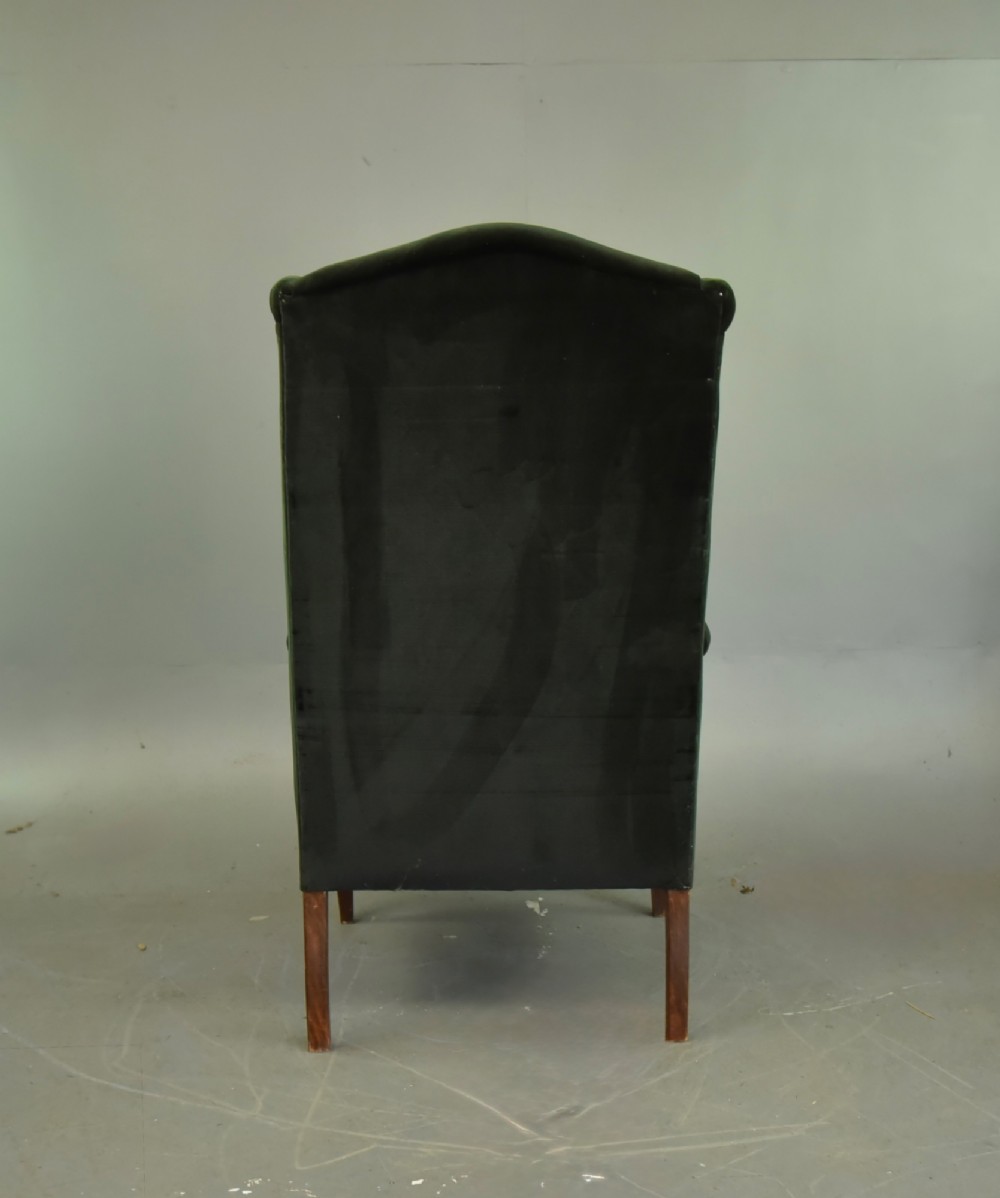 An Edwardian mahogany wing armchair upholstered in dark green velvet with contrasting decorative gimp trim and tapered front legs. View V
