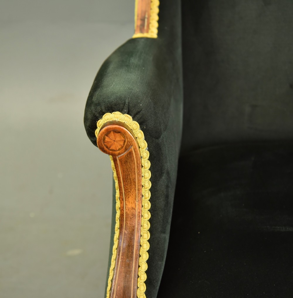 An Edwardian mahogany wing armchair upholstered in dark green velvet with contrasting decorative gimp trim and tapered front legs. View VI