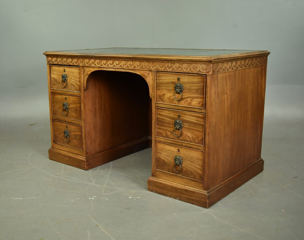 A 19th-century Regency style mahogany pedestal desk featuring a leather writing top, carved wave frieze, six drawers with brass lion mask handles, and a central kneehole aperture. View II