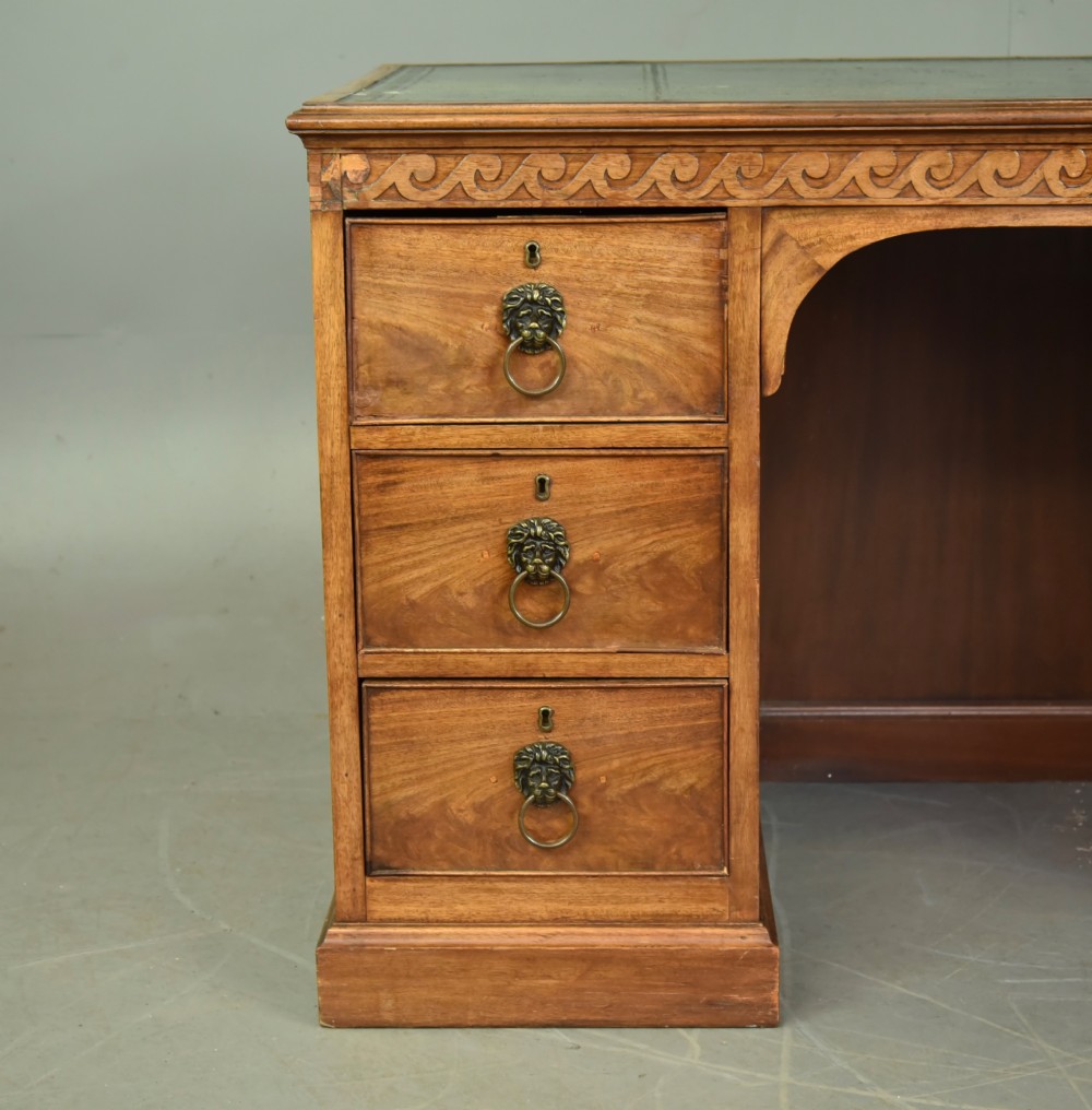 A 19th-century Regency style mahogany pedestal desk featuring a leather writing top, carved wave frieze, six drawers with brass lion mask handles, and a central kneehole aperture. View III