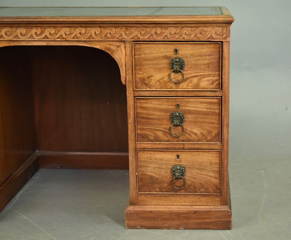 A 19th-century Regency style mahogany pedestal desk featuring a leather writing top, carved wave frieze, six drawers with brass lion mask handles, and a central kneehole aperture. View IV