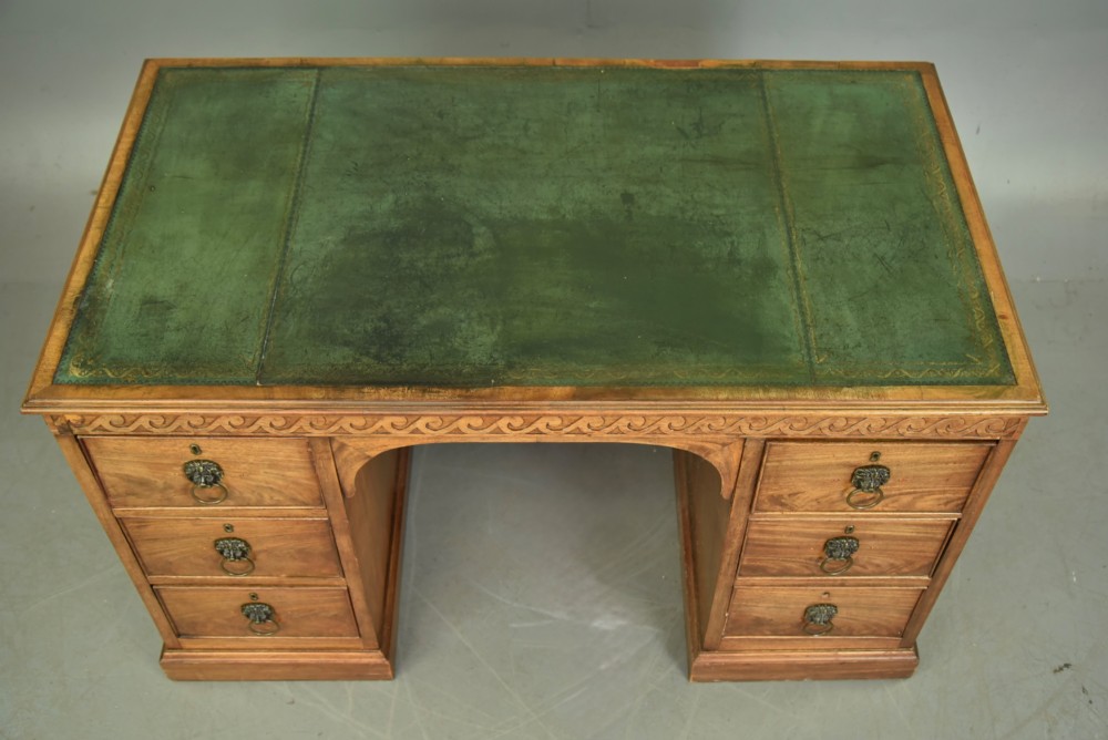 A 19th-century Regency style mahogany pedestal desk featuring a leather writing top, carved wave frieze, six drawers with brass lion mask handles, and a central kneehole aperture. View V