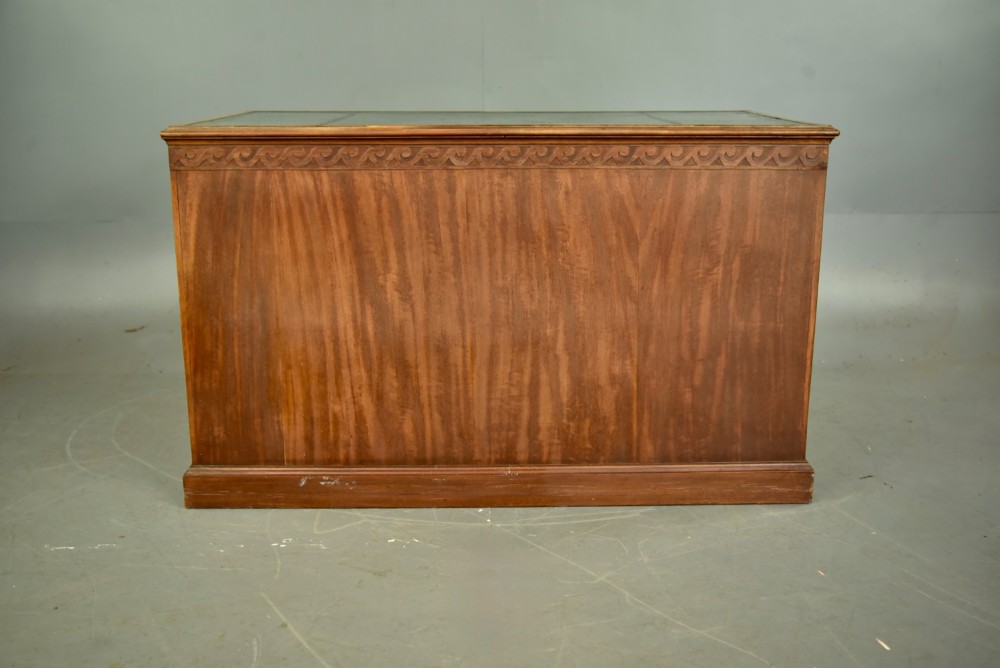 A 19th-century Regency style mahogany pedestal desk featuring a leather writing top, carved wave frieze, six drawers with brass lion mask handles, and a central kneehole aperture. View VI
