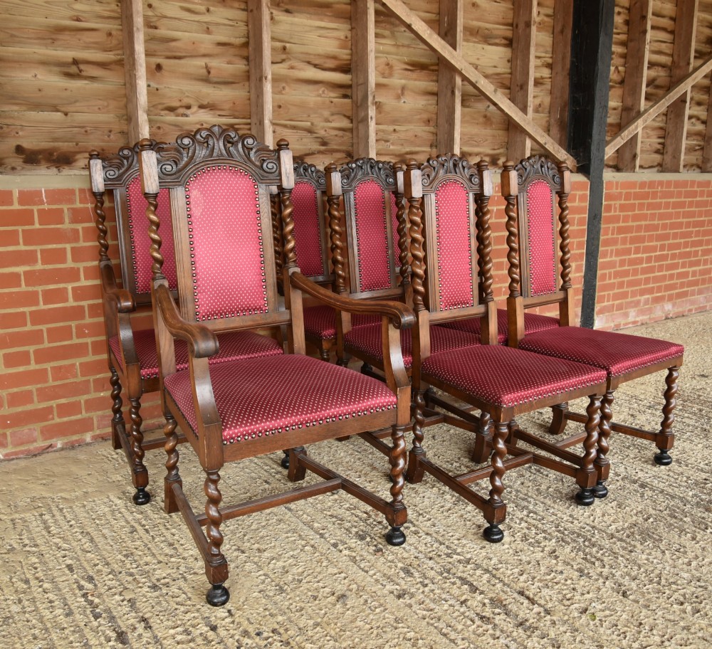 A set of eight carved oak dining chairs featuring barley twist supports, high carved crests, and red upholstered seats and backrests with brass stud detailing. View II