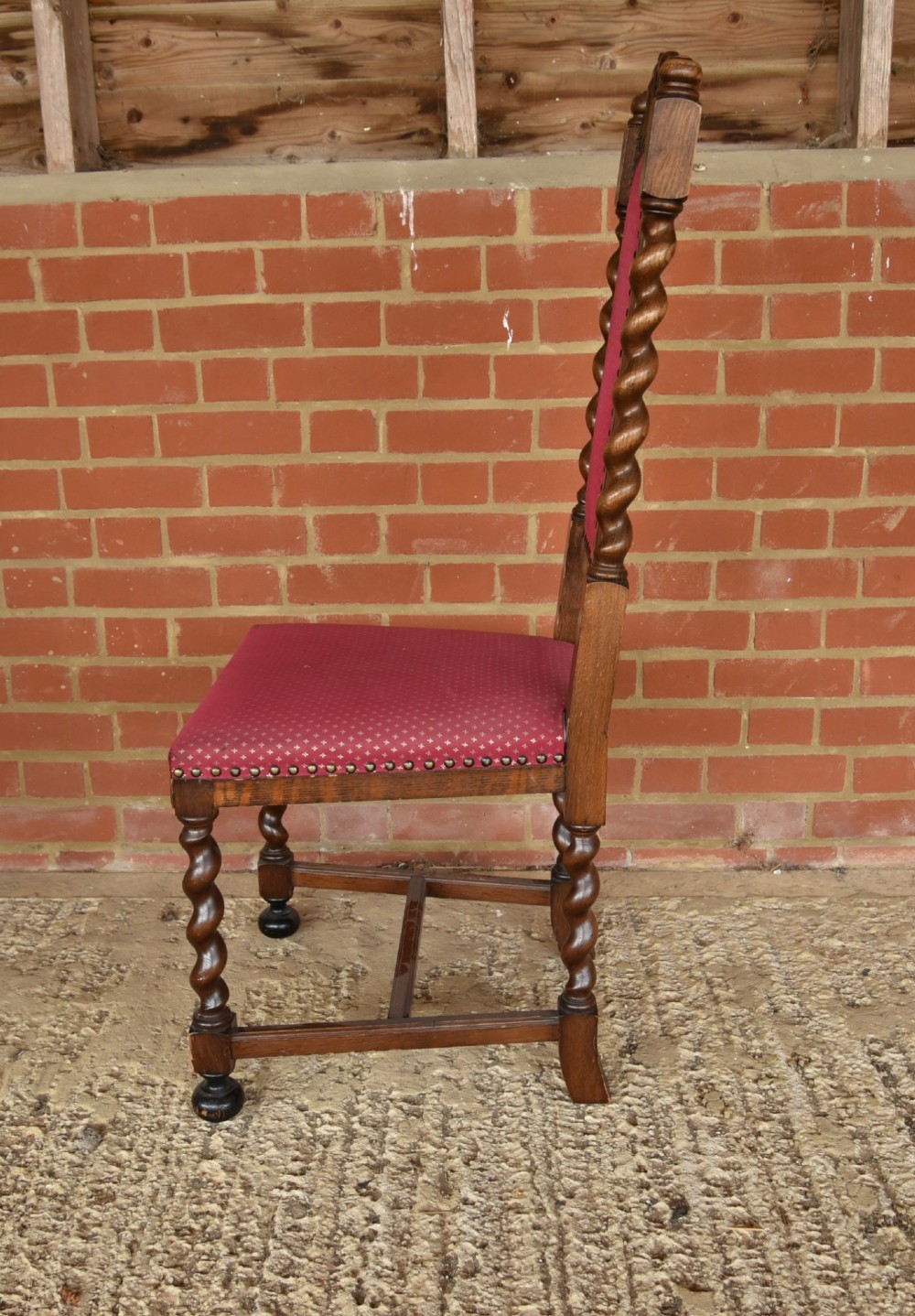 A set of eight carved oak dining chairs featuring barley twist supports, high carved crests, and red upholstered seats and backrests with brass stud detailing. View IV
