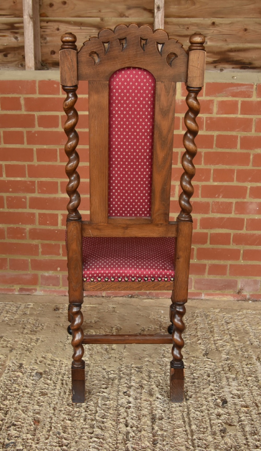 A set of eight carved oak dining chairs featuring barley twist supports, high carved crests, and red upholstered seats and backrests with brass stud detailing. View V