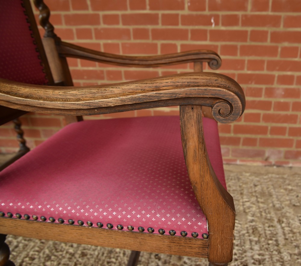 A set of eight carved oak dining chairs featuring barley twist supports, high carved crests, and red upholstered seats and backrests with brass stud detailing. View IX