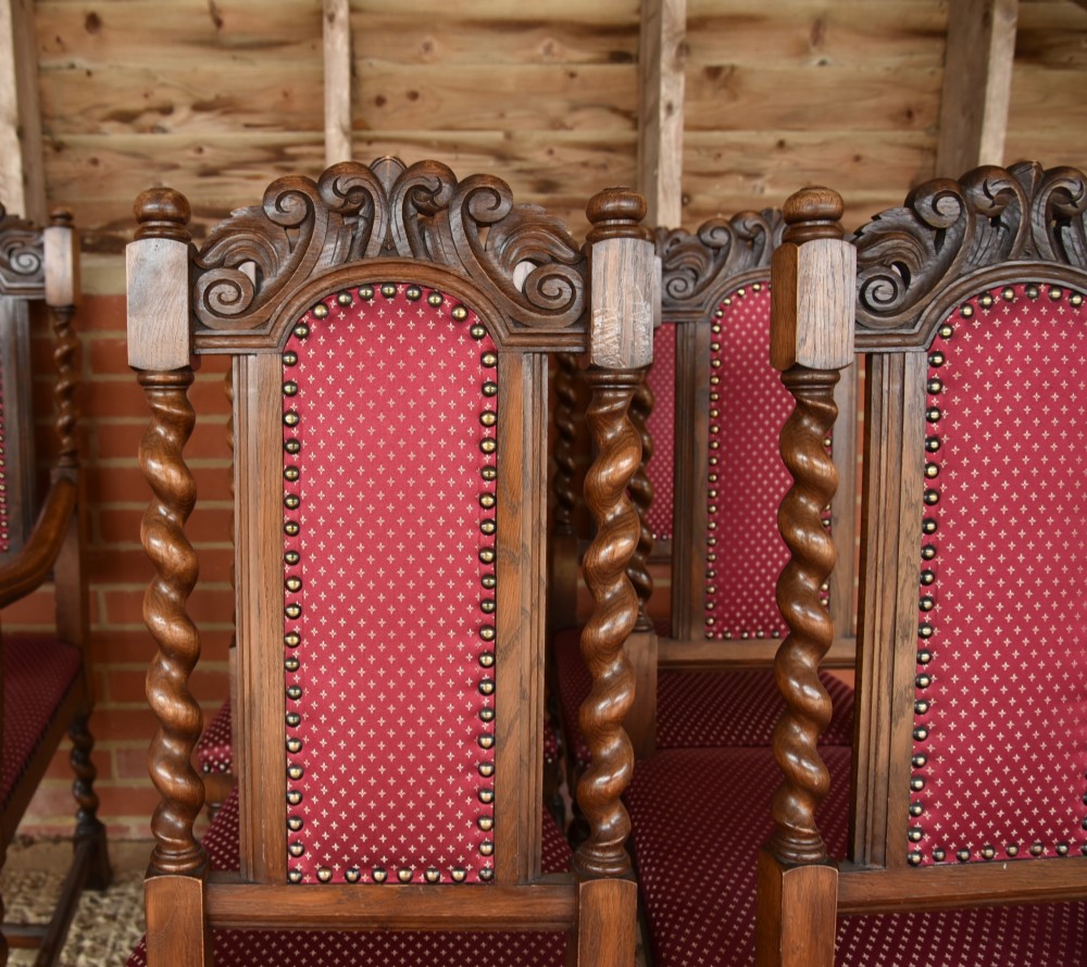 A set of eight carved oak dining chairs featuring barley twist supports, high carved crests, and red upholstered seats and backrests with brass stud detailing. View XI