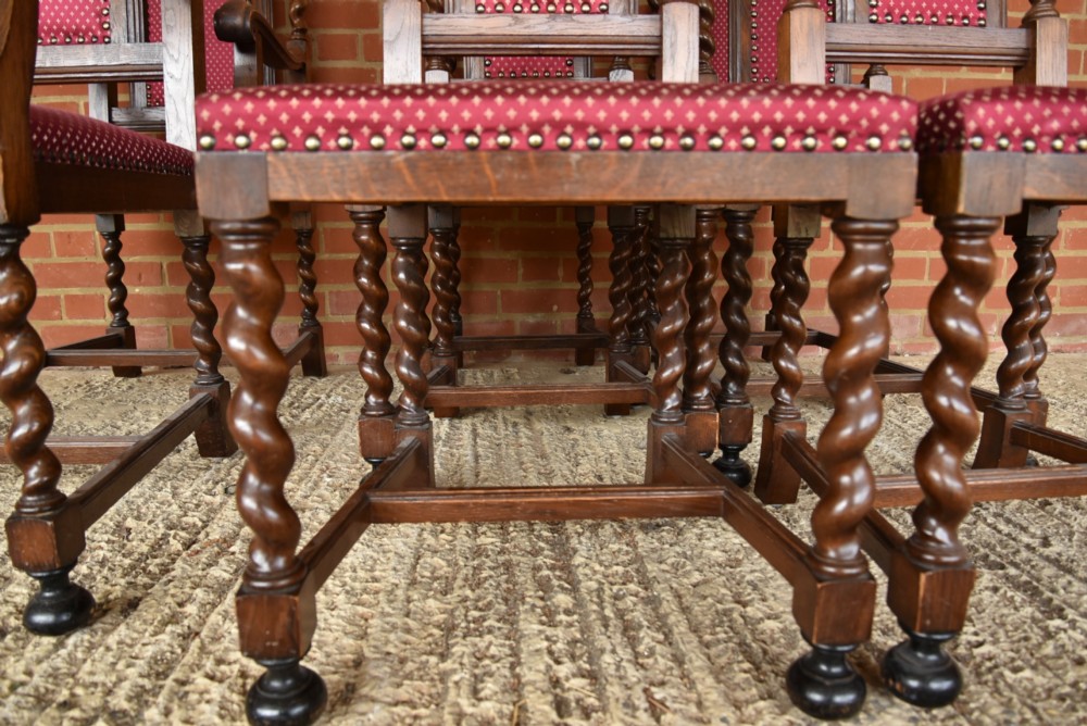 A set of eight carved oak dining chairs featuring barley twist supports, high carved crests, and red upholstered seats and backrests with brass stud detailing. View XII