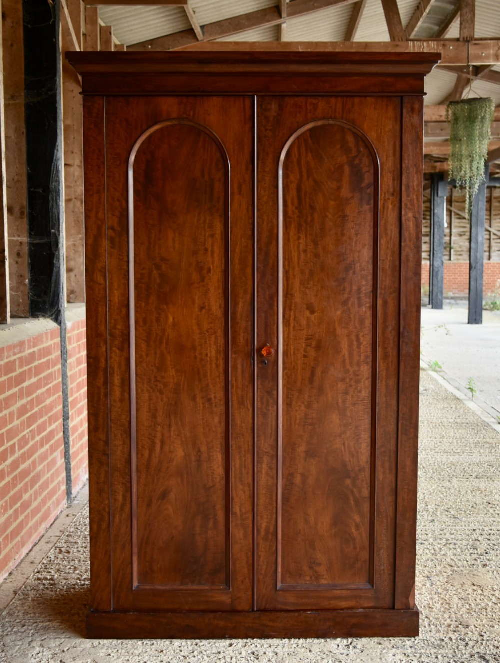 A Victorian mahogany double wardrobe featuring two arched panel doors, a moulded top cornice, and a solid plinth base.