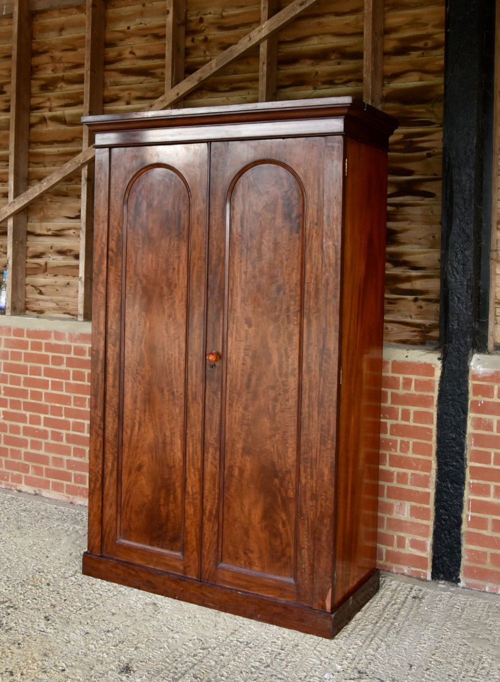 A Victorian mahogany double wardrobe featuring two arched panel doors, a moulded top cornice, and a solid plinth base. View II