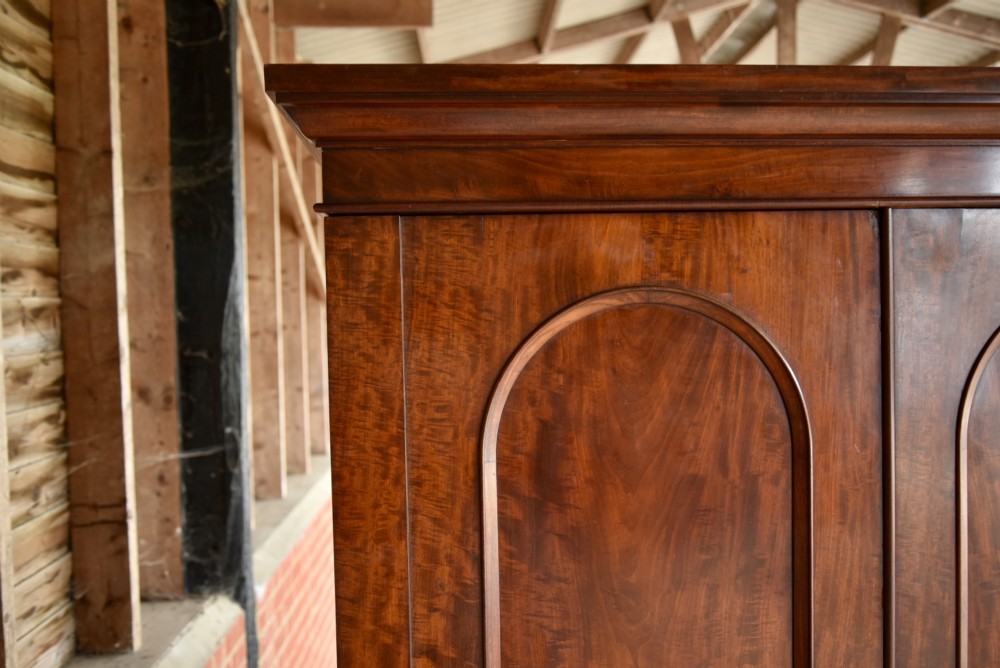 A Victorian mahogany double wardrobe featuring two arched panel doors, a moulded top cornice, and a solid plinth base. View III