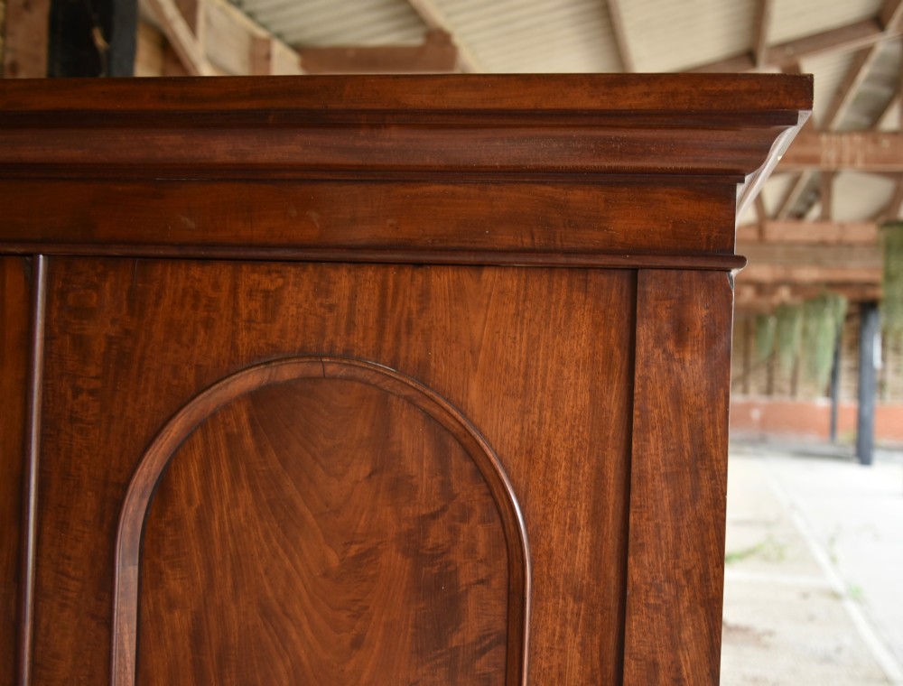 A Victorian mahogany double wardrobe featuring two arched panel doors, a moulded top cornice, and a solid plinth base. View IV