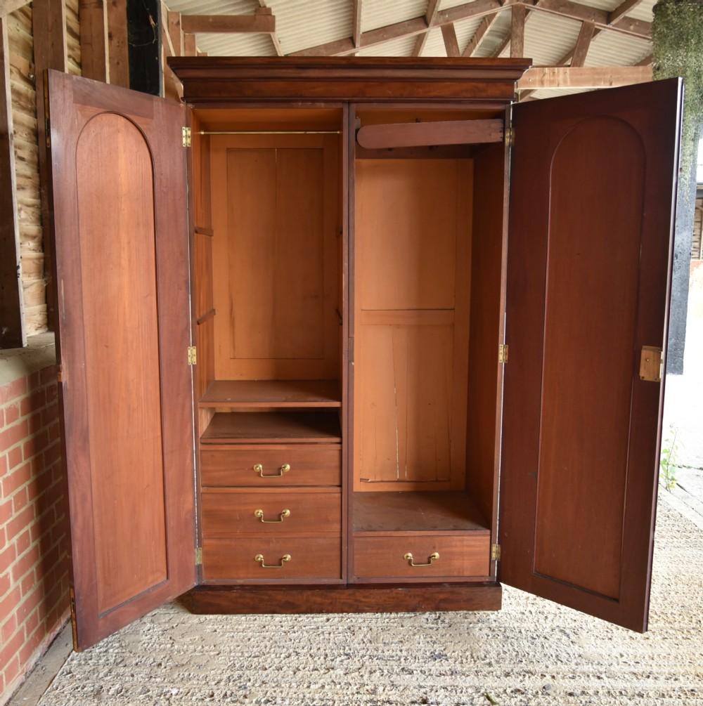 A Victorian mahogany double wardrobe featuring two arched panel doors, a moulded top cornice, and a solid plinth base. View V