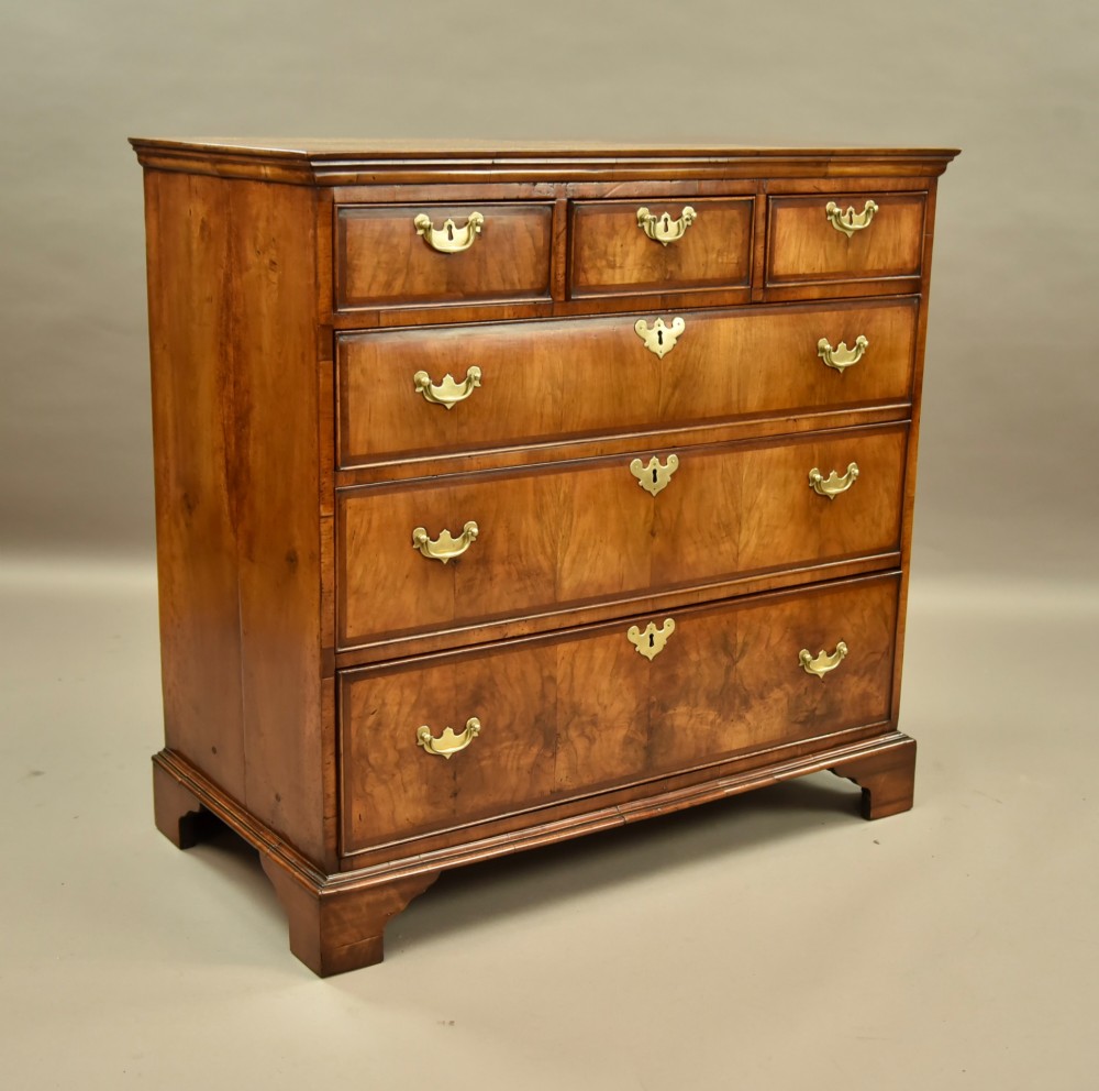 An 18th-century Georgian walnut chest of drawers featuring three short drawers over three long graduated drawers with brass handles and bracket feet. View II