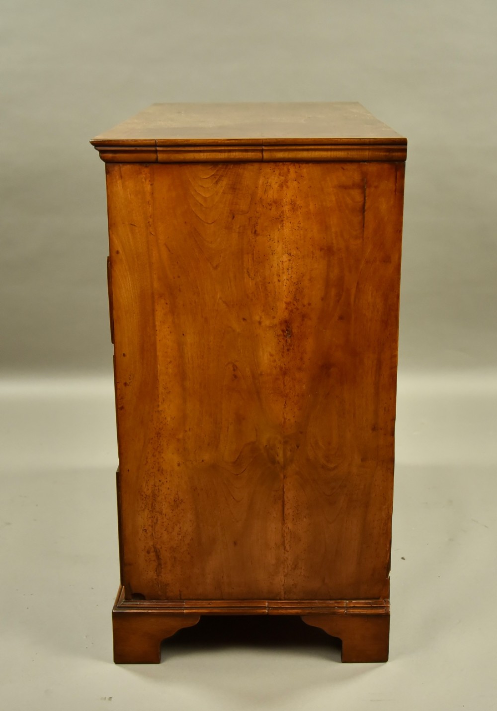 An 18th-century Georgian walnut chest of drawers featuring three short drawers over three long graduated drawers with brass handles and bracket feet. View IV