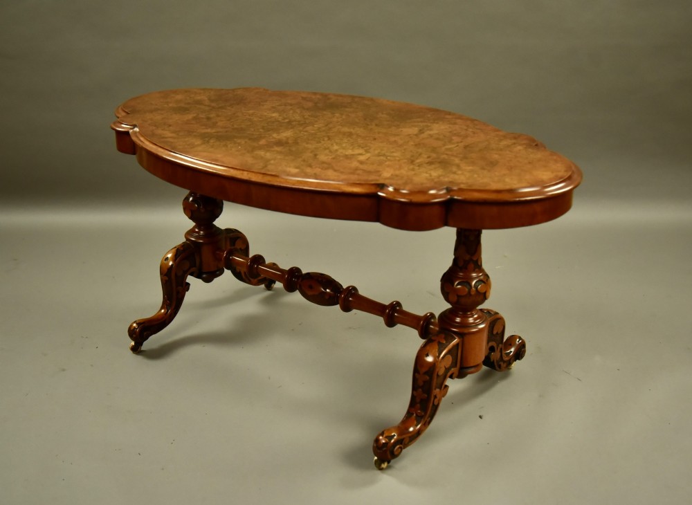A Victorian burr walnut low coffee table featuring a shaped serpentine top, turned stretcher base, and inlaid legs on brass castors.